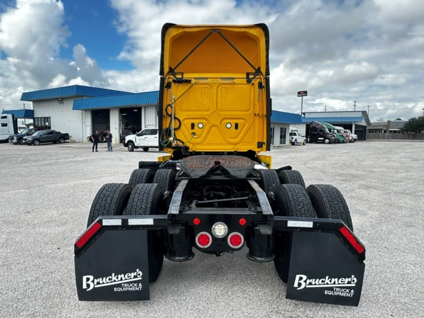 Truck rear view of a 2019 Freightliner Cascadia 126 day cab with fifth wheel, yellow cab, dual rear axles, mud flaps labeled Bruckner’s Equipment, in a dealership lot.