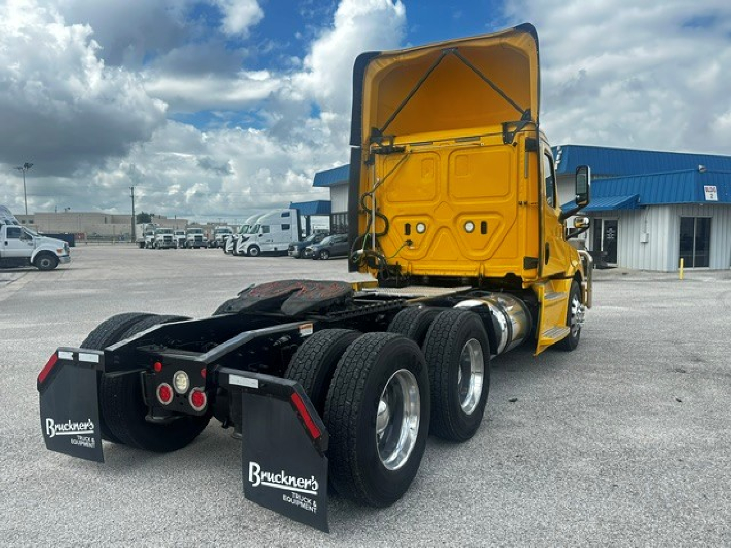 Freightliner Cascadia 126 tractor show view from rear with yellow cab and opened sleeper/roof hatch, dual rear axles, black chassis, and mud flaps.