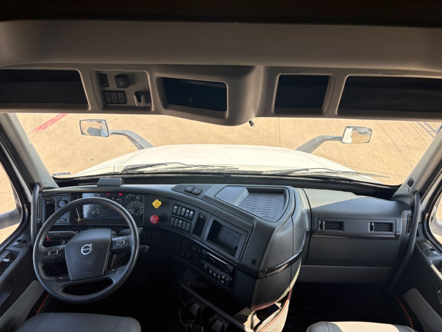 Volvo VNR cab interior showing steering wheel, dashboard controls, and windshield with side mirrors.