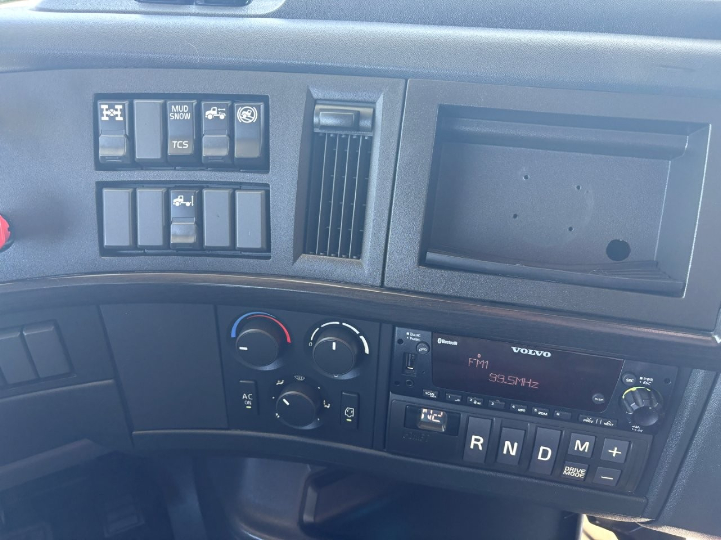 Dashboard area of a Volvo VNR truck showing control switches, climate controls, radio, and gear selector with R N D M indicators.