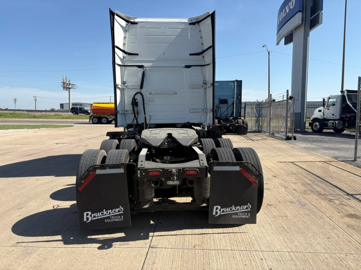 Truck rear-view showing fifth wheel and dual rear axles with mud flaps labeled Bruckner Equipment. Volvo dealer sign visible in background.