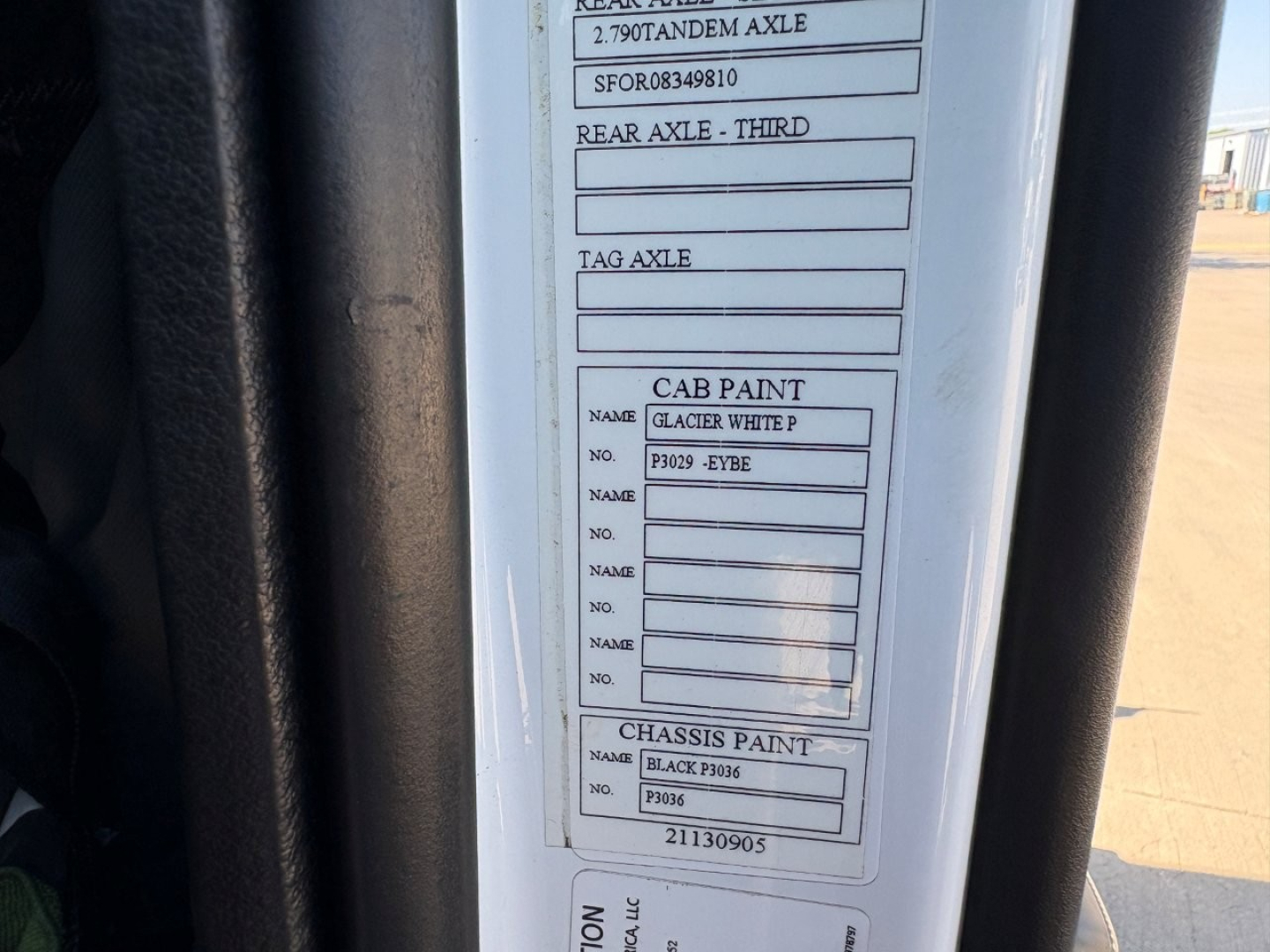 Truck cab door sticker with paint codes and axle specs visible, including rear axle, tag axle, cab paint Glacier White, chassis paint Black F306, serial numbers and lot data.