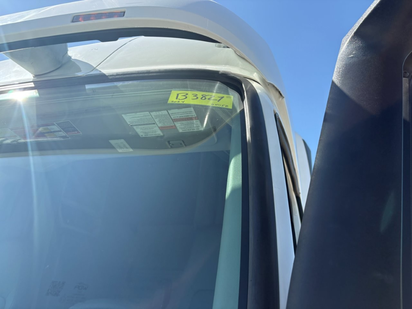 Truck cab window with yellow stock tag  B3827 visible in windshield, partial cab roof and side mirror, 2024 Volvo VNR64T660 listing.