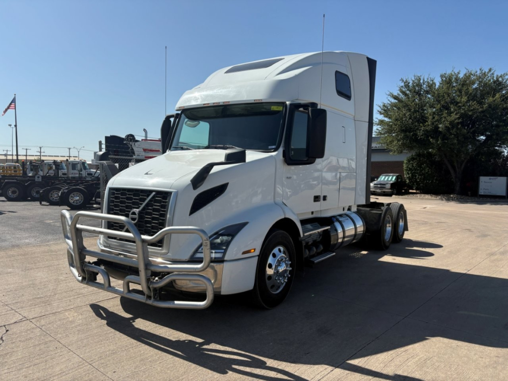 Volvo VNR64T660 conventional sleeper truck in a parking lot, white exterior, large grille with bull bar, dual rear axles, driver-side door, stacked fuel tanks.
