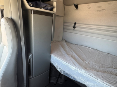 Interior sleeper cab of a Volvo VNR truck showing a single bunk bed with mattress and a small cabinet/refrigerator unit beside it.