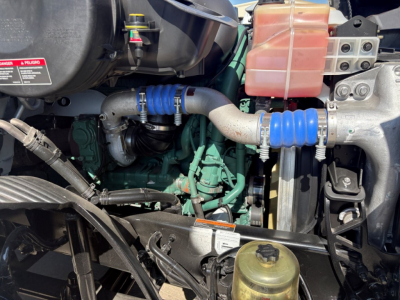 Volvo VNR truck engine bay showing blue silicone hose connections, coolant reservoir, and various engine components.