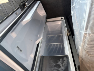 Truck cab area showing an open under-dash refrigerator/freezer unit with empty shelves inside a Volvo VNR64T660 sleeper cab, compact interior view