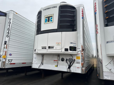 Thermo King unit on front of refrigerated trailer with white body, black grille, and logos; side rails and other trailers visible, hydraulic lines and electrical hookups at bottom.