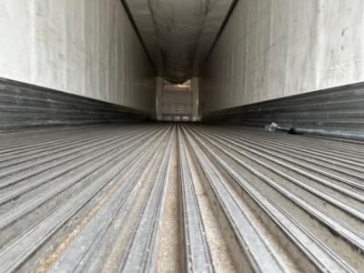 Trailer interior showing ribbed steel floor in a long empty refrigerated trailer with light at far end.
