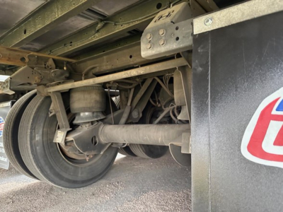 Trailer undercarriage showing wheel, axle, suspension components, and part of the frame in a utilities trailer.
