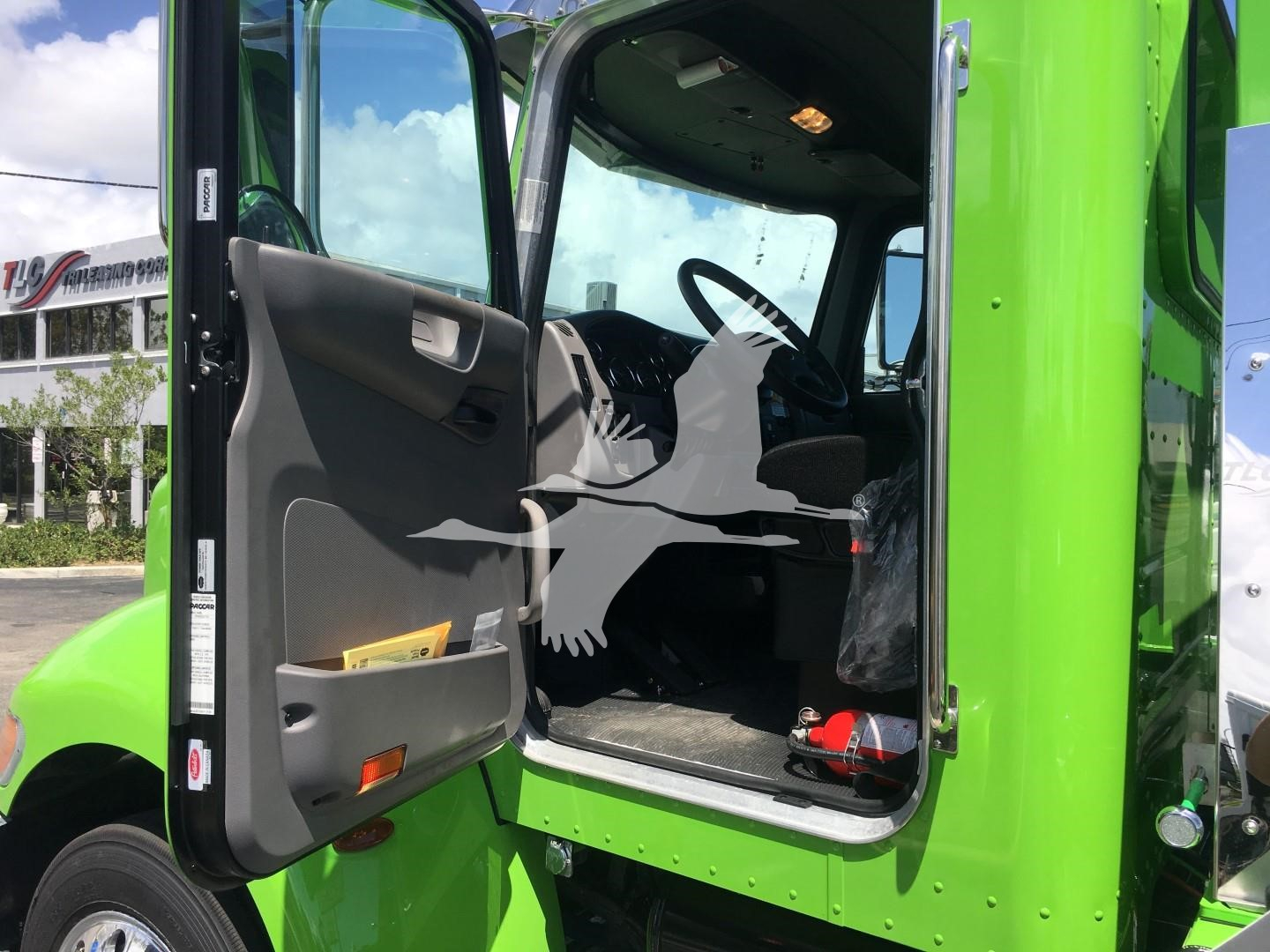 Truck cab interior of a 2022 Peterbilt 337 in a bright green color, driver's door open showing steering wheel, dashboard, and seating; stock number J52310 listing information overlay.