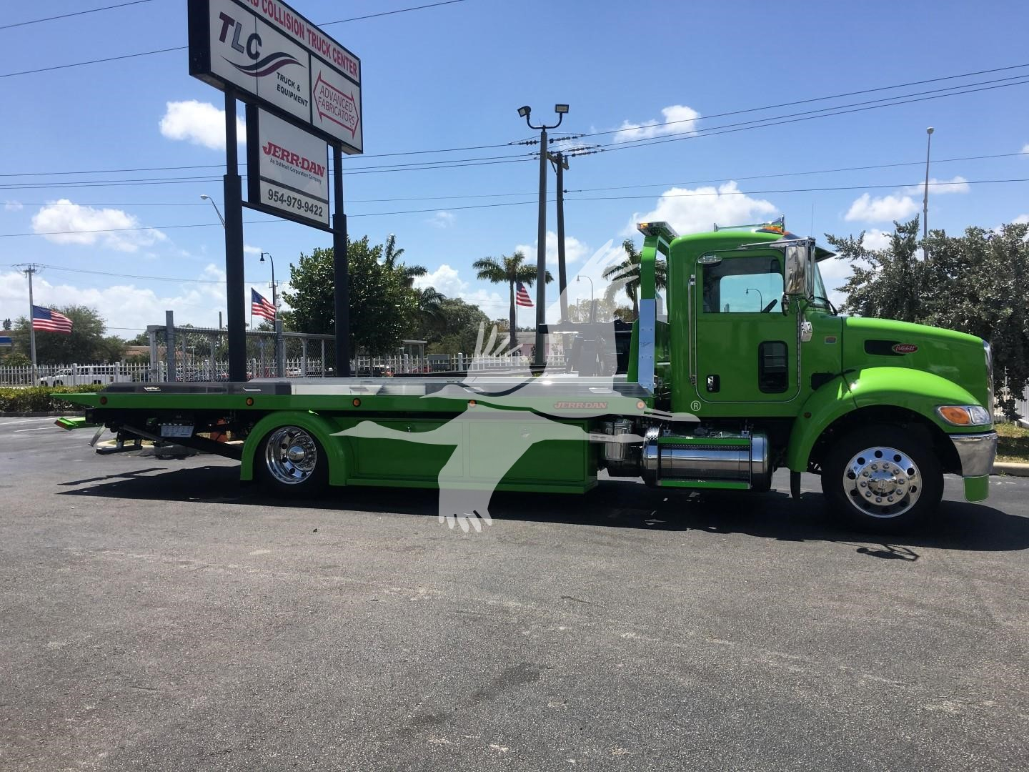 Green tow truck with flatbed shown in side view, Peterbilt 337 chassis, low ground clearance, chrome wheels, day-lit outdoor lot.
