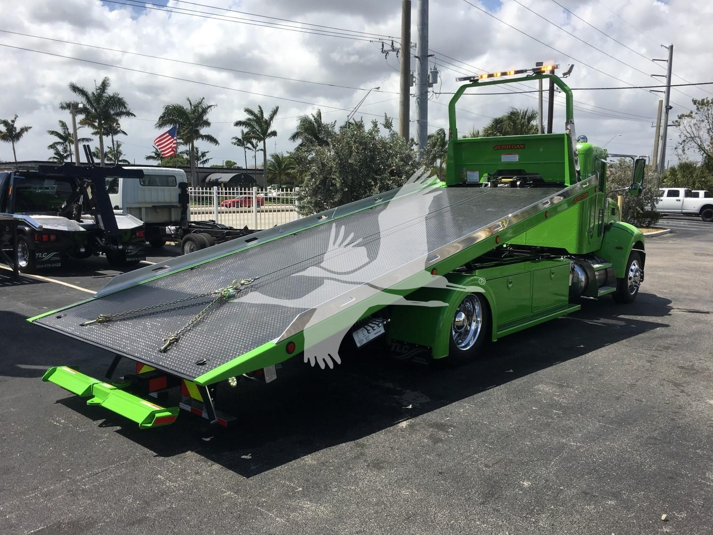 Green 2022 Peterbilt 337 rollback tow truck with tilted metallic ramp in a dealership lot, stock number J52310, new vehicle.