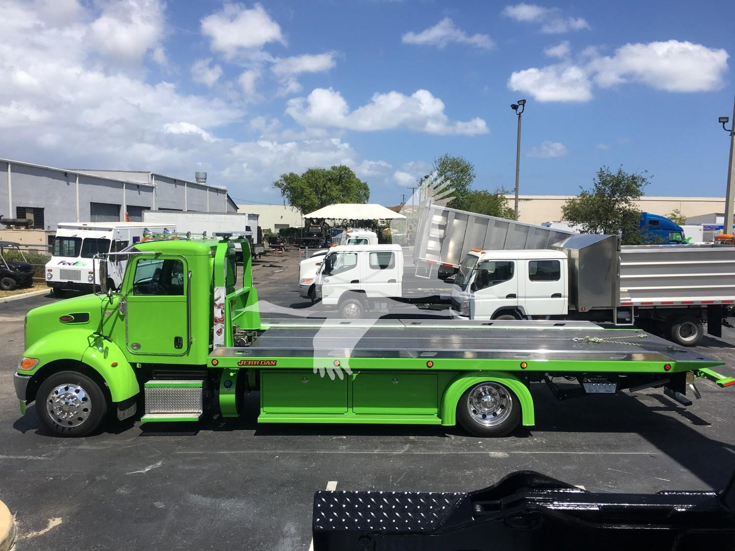 Green Peterbilt 337 rollback tow truck side view with flatbed and chrome accents; text on truck panels not clearly legible.