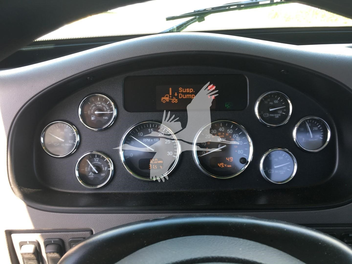 Dashboard of a 2022 Peterbilt 337 with multiple round gauges and a digital display showing a warning icon; visible text includes 'Suspended Dump' icon on center screen.