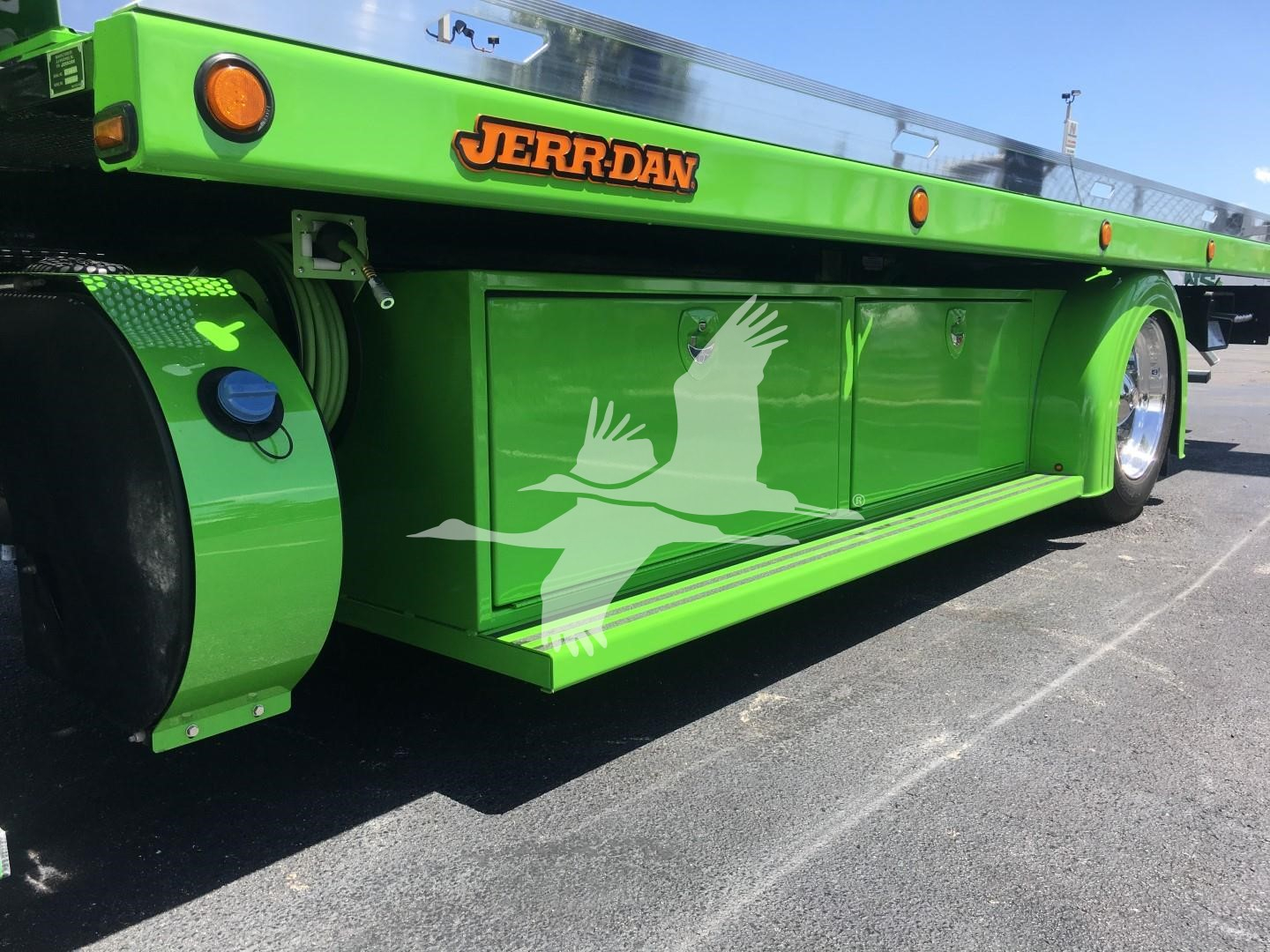 Green Peterbilt rollback truck side with cargo box and JERR-DAN logo, graphic of white flying bird on lower side panel.