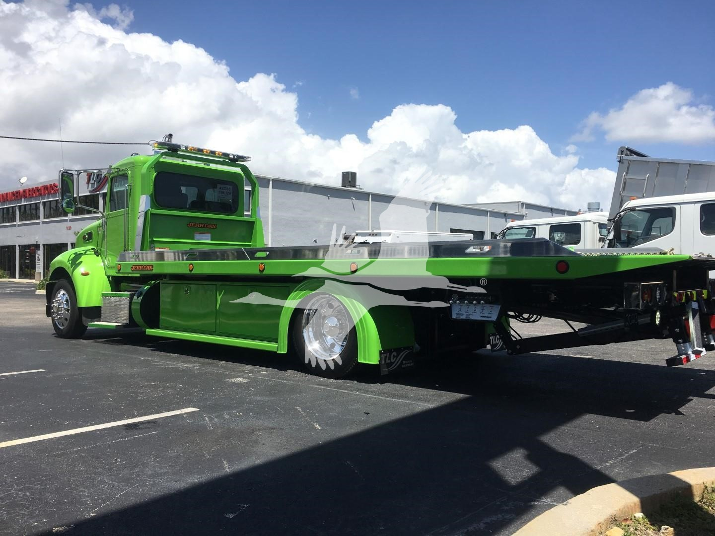 Green Peterbilt 337 rollback tow truck parked in lot, side view showing flatbed and compartments, stock number J52310.