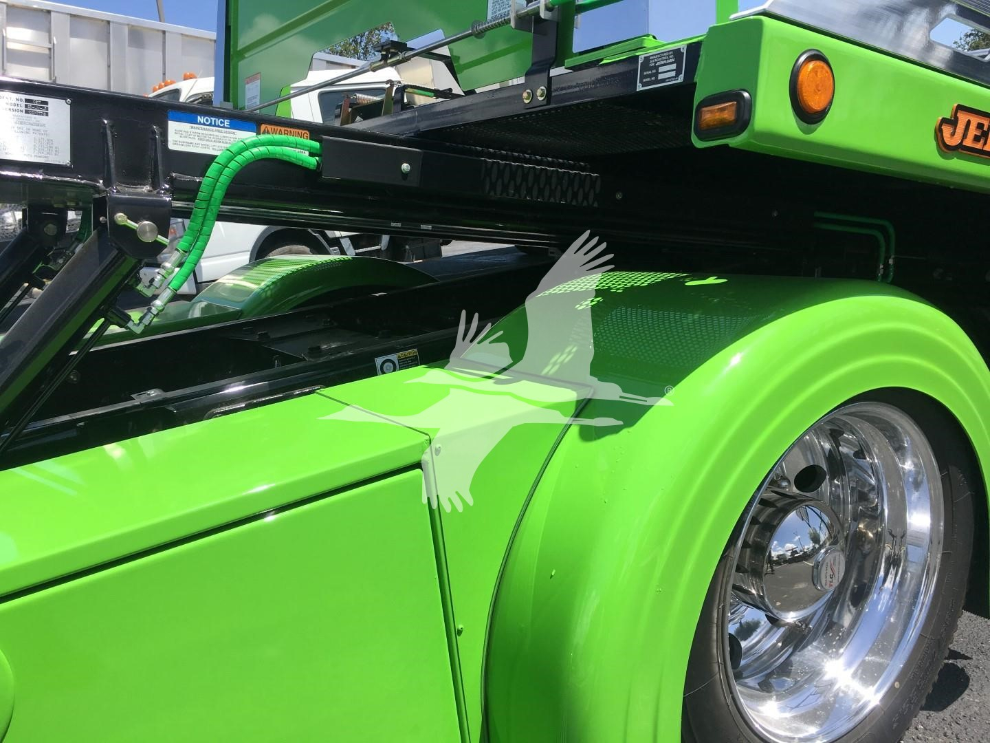 Peterbilt 337 rollback truck wheel and bright green fender with chrome wheel, hydraulic hoses and bed frame visible.