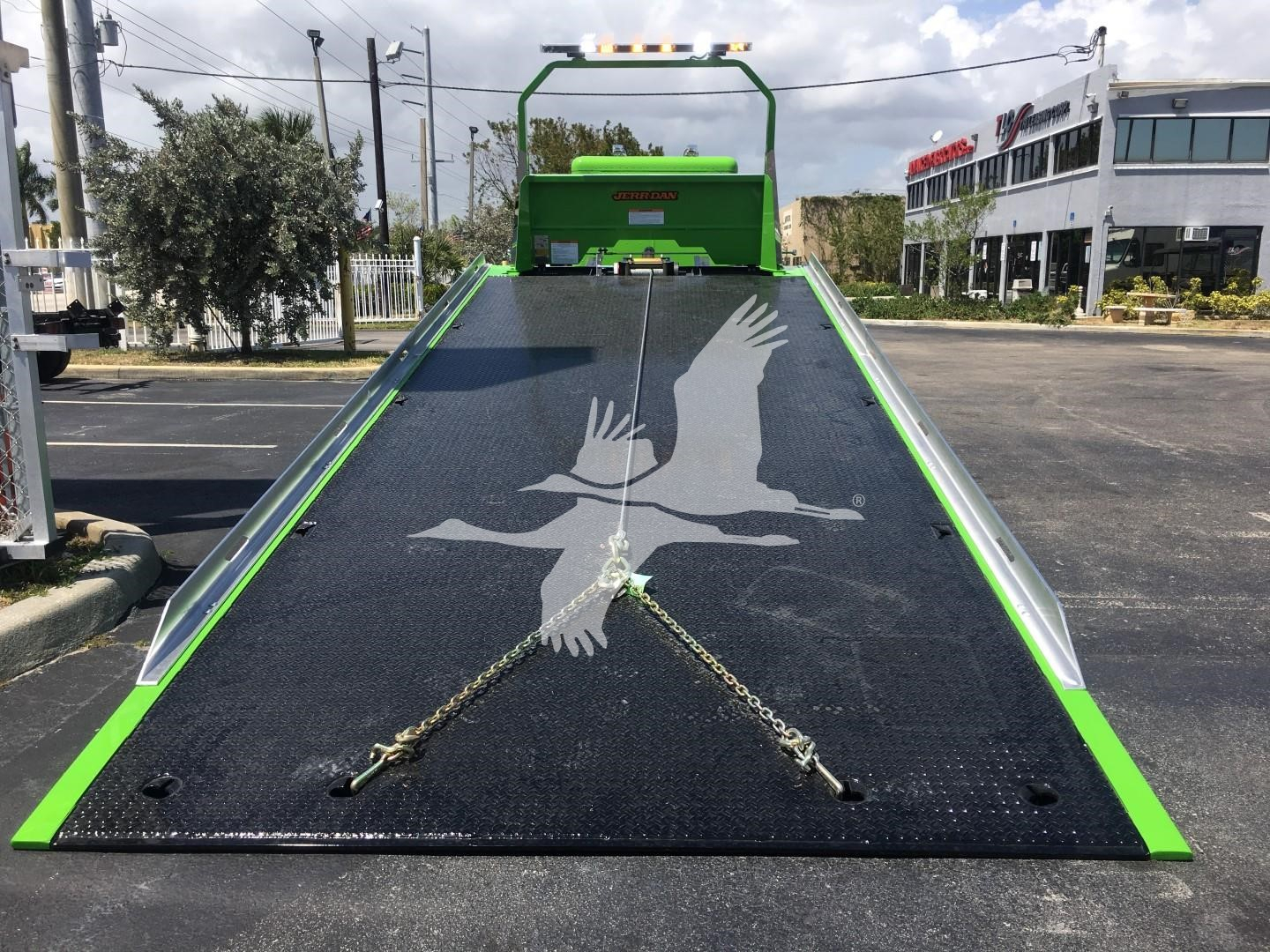 Peterbilt 337 rollback truck in black flatbed with green accents and white crane birds logo on loading ramp.
