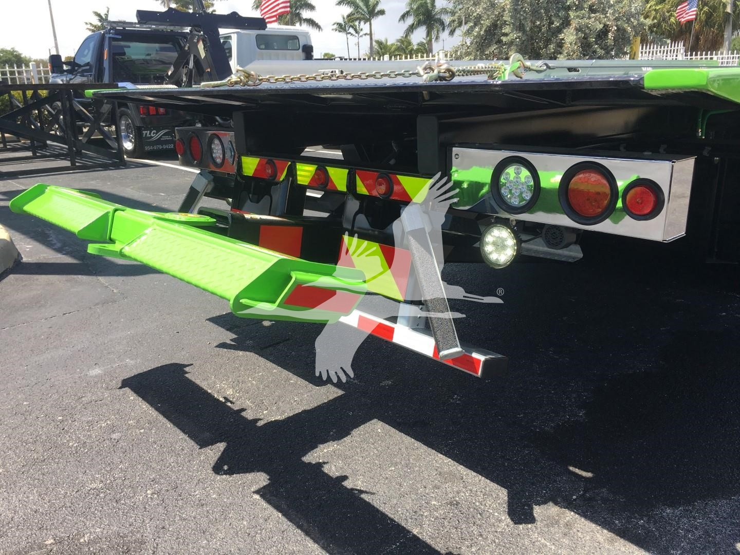 Back of green Peterbilt 337 rollback truck showing fold-down green ramp and rear lighting and reflectors.