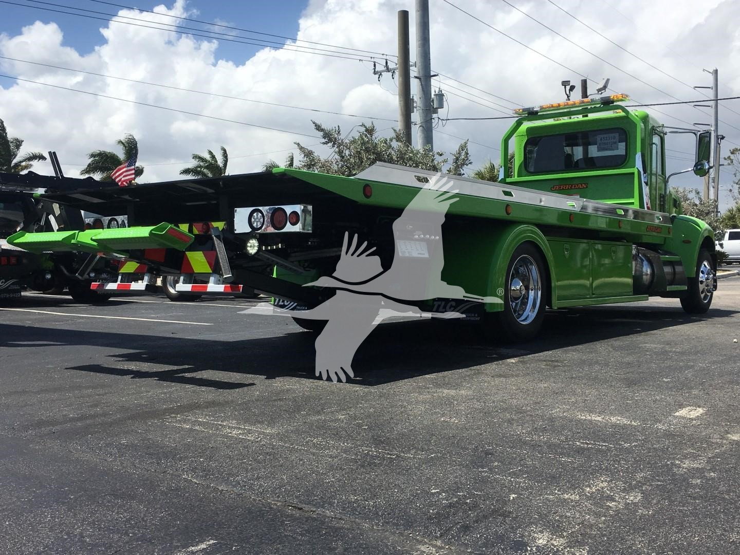 Green Peterbilt 337 rollback tow truck with flatbed, front cab and extended bed visible.