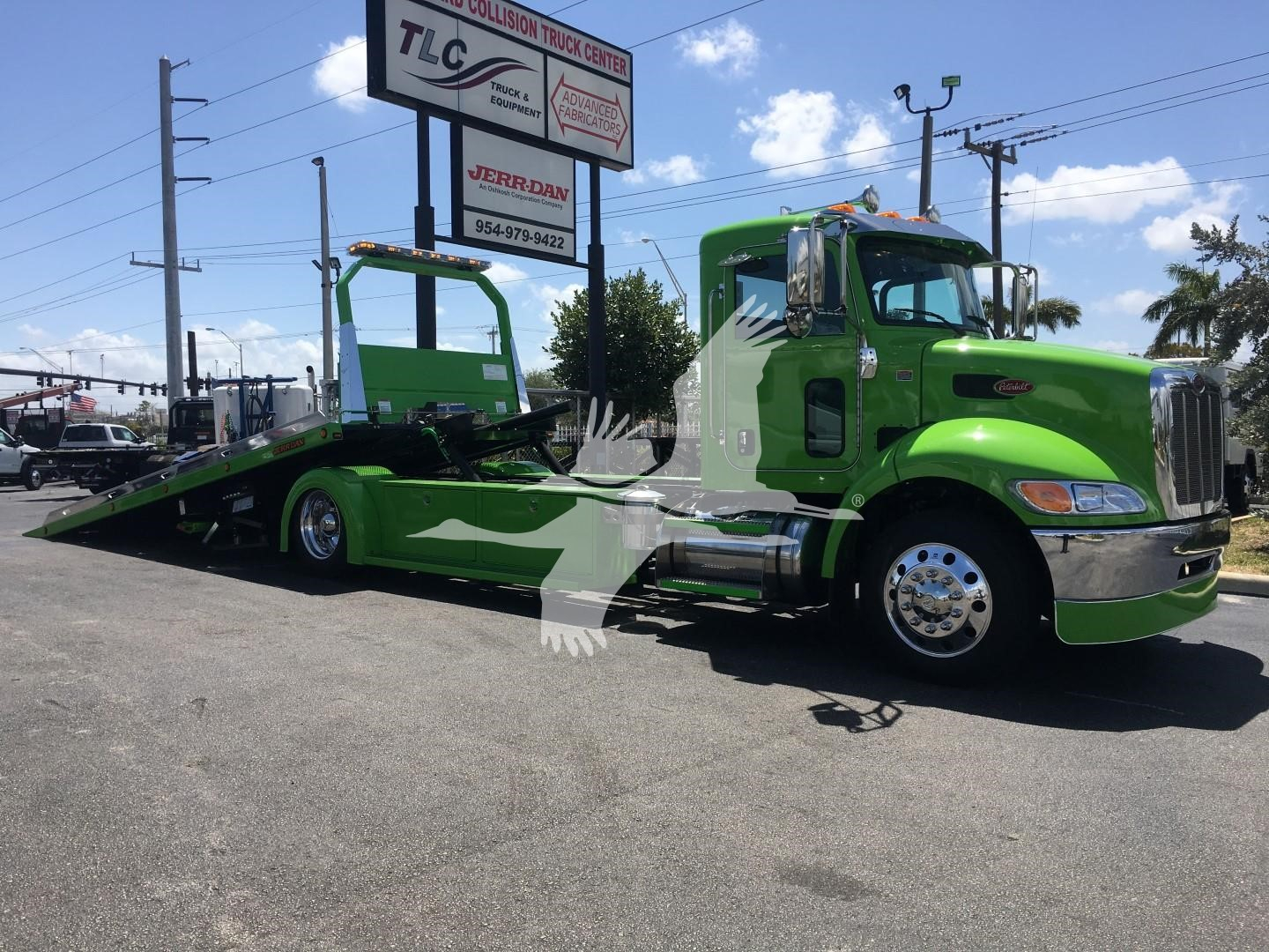 Green Peterbilt 337 rollback tow truck in a dealership lot, side view with a low-profile tow bed, TLC/Jerr-Dan signs in background.