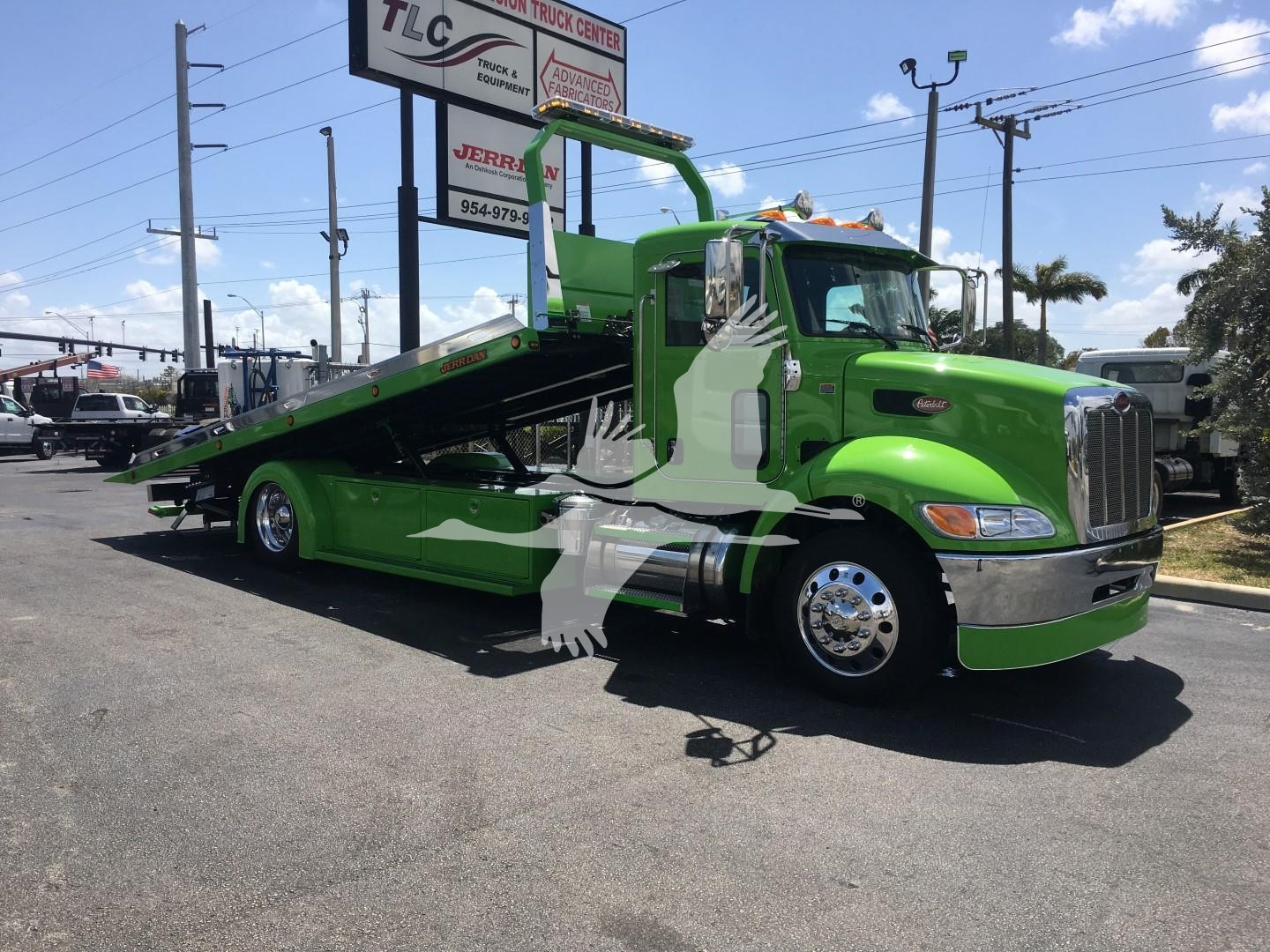 Green Peterbilt 337 rollback tow truck parked in lot showing tilt bed and chrome bumper
