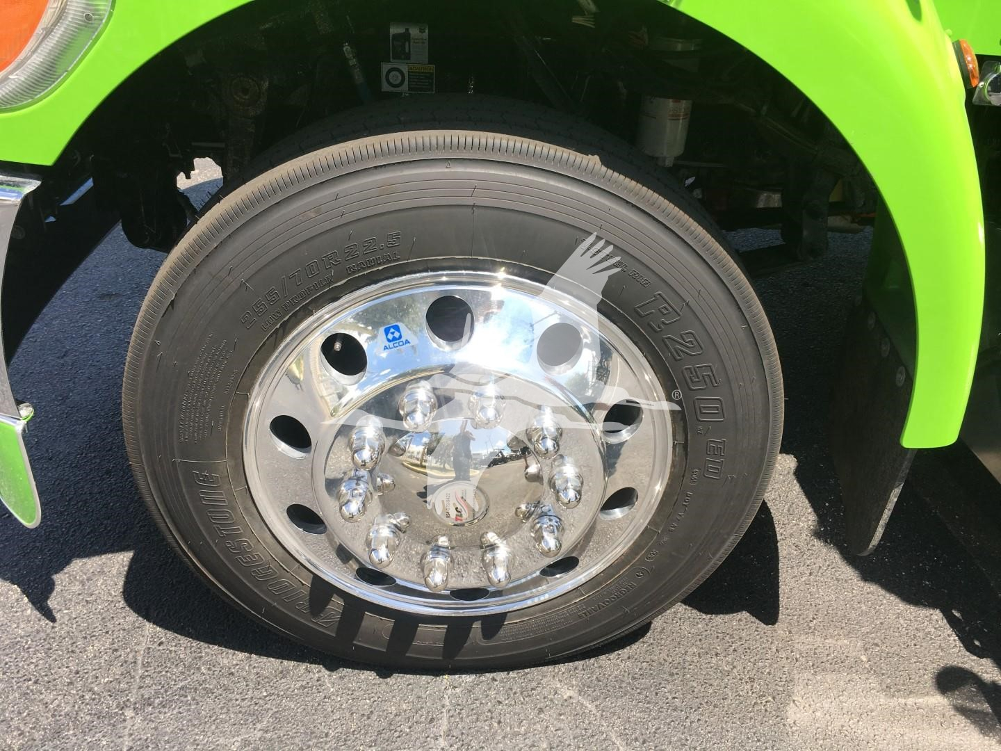 Truck wheel close-up showing chrome hub and tire with Peterbilt wheel cover, green fender in background.
