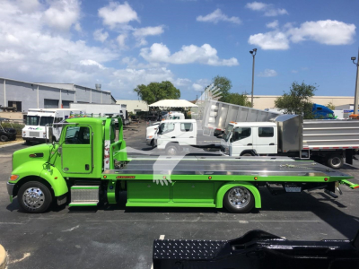 Green Peterbilt 337 rollback tow truck side view with flatbed and chrome accents; text on truck panels not clearly legible.