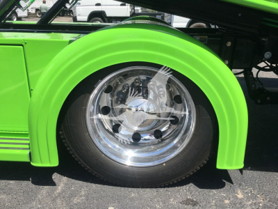 Front wheel area of a bright green Peterbilt 337 rollback truck showing chrome wheel and green fender.