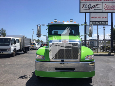 Peterbilt 337 truck front view in bright green color with chrome grille and bumper, daytime dealership lot background with signs.