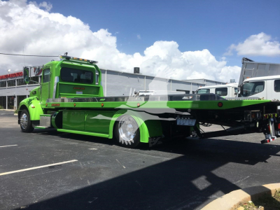 Green Peterbilt 337 rollback tow truck parked in lot, side view showing flatbed and compartments, stock number J52310.
