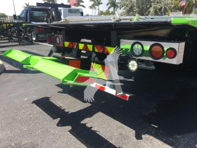 Back of green Peterbilt 337 rollback truck showing fold-down green ramp and rear lighting and reflectors.