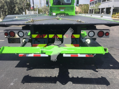 Rear view of a green Peterbilt rollback truck showing taillights, bumper, and platform with safety markings and lights.