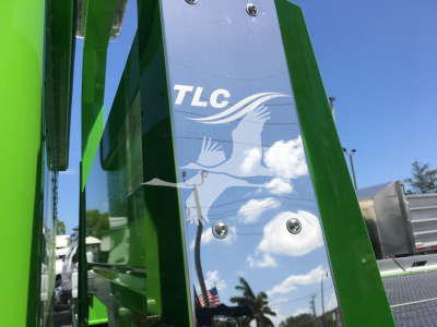 Green Peterbilt 337 rollback truck component with TLC logo and white graphic on blue panel, clear sky background