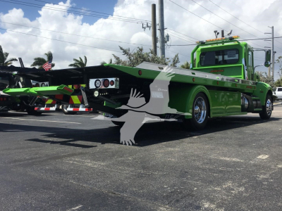 Green Peterbilt 337 rollback tow truck with flatbed, front cab and extended bed visible.