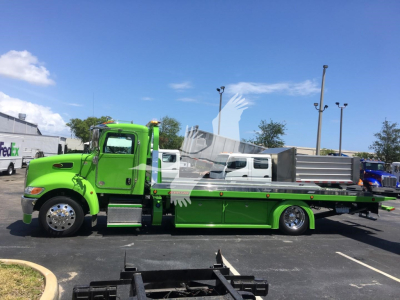 Green Peterbilt 337 rollback tow truck side view. Visible text includes stock number J52310 on dealership tag.