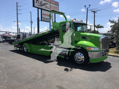 Green Peterbilt 337 rollback tow truck parked in lot showing tilt bed and chrome bumper