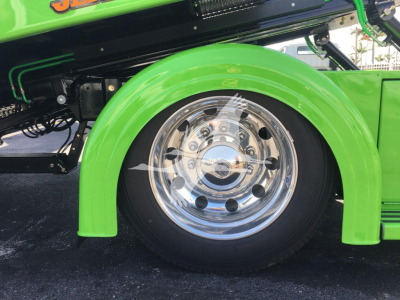 Green Peterbilt 337 rollback truck wheel area with chrome hubcap and fender; partial dealership graphics.