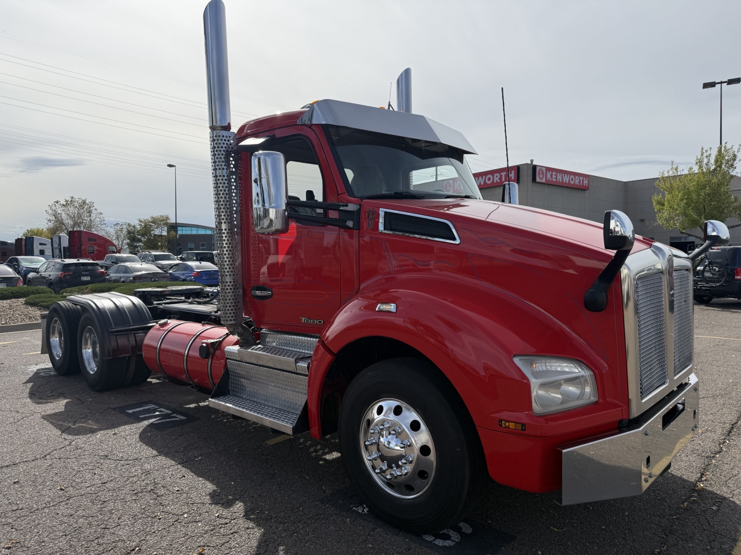 Kenworth T880 conventional daycab truck in red, side view showing chrome exhaust stacks, fuel tanks, and front grille; no visible text aside from model styling.