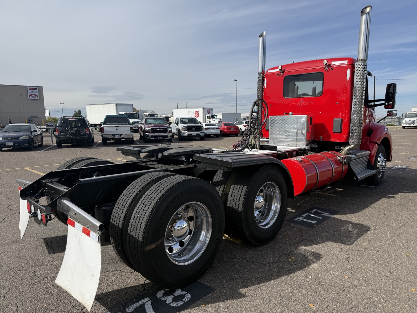 Kenworth T880 conventional daycab tractor in red, viewed from rear-left with dual rear axles and fifth-wheel absence. Visible tires, chrome wheels, and exhaust stacks.