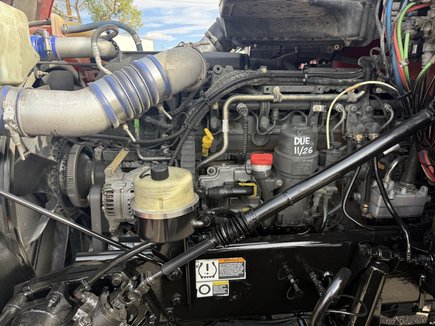 Kenworth T880 engine bay showing coolant reservoir, hoses, wiring, and diesel engine components.