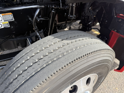 Kenworth T880 wheel and front suspension area showing tire treads and rim, with portions of the truck frame and hydraulic lines in view.