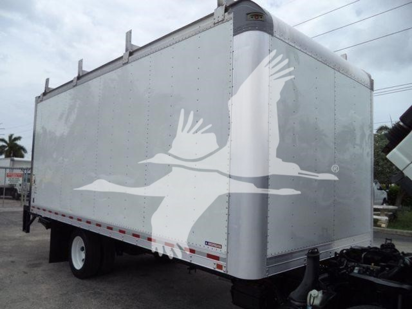 Isuzu NPR HD box truck trailer showing plain aluminum cargo body with logo silhouettes of flying birds on the side.