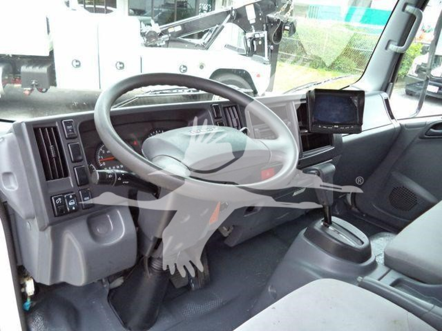 Isuzu NPR HD cab interior showing steering wheel, dashboard, gear shifter, and steering column with mounted screen.