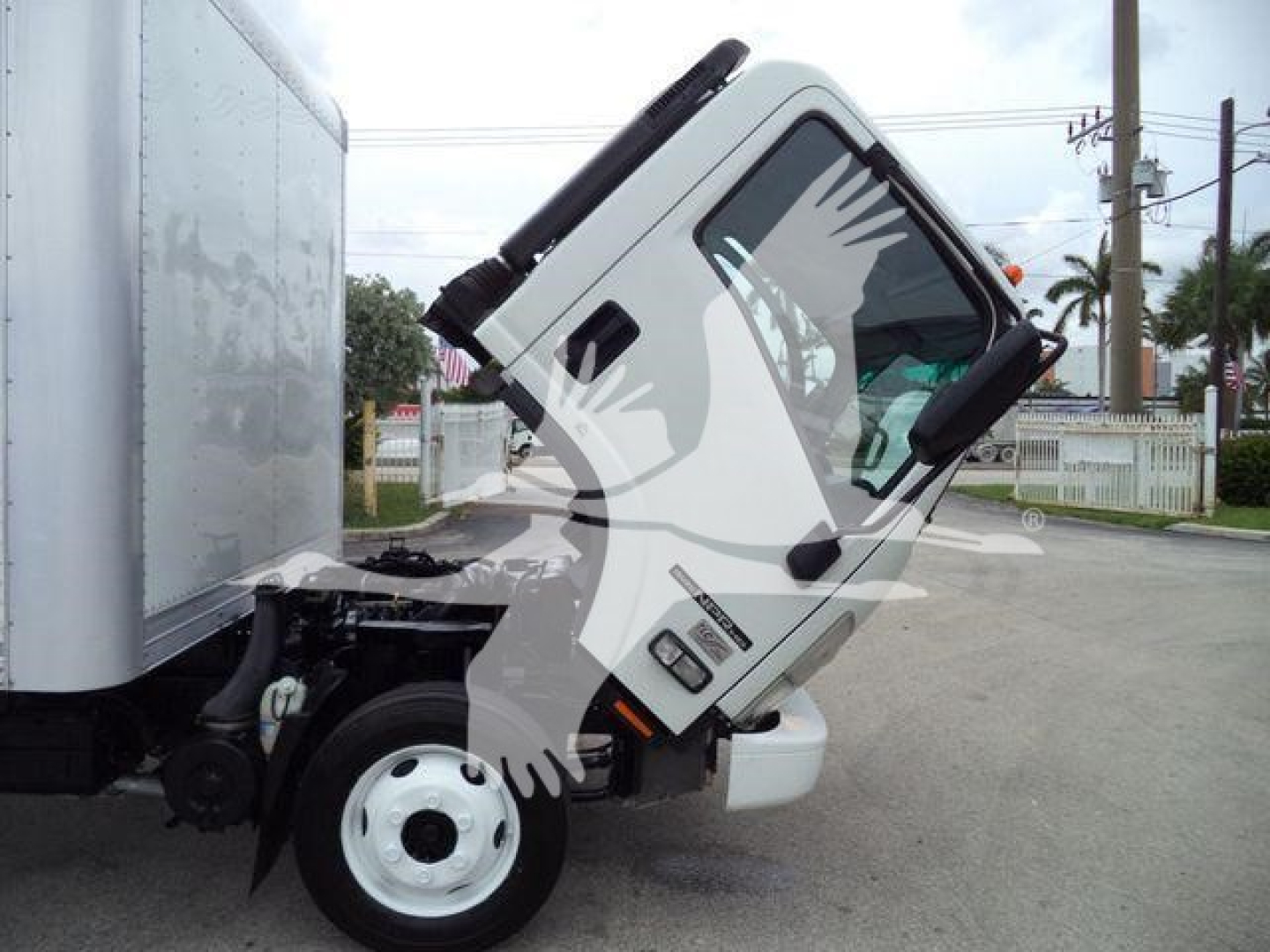 Isuzu NPR HD truck cab tilted upward showing side view with box trailer; front bumper and wheel visible.