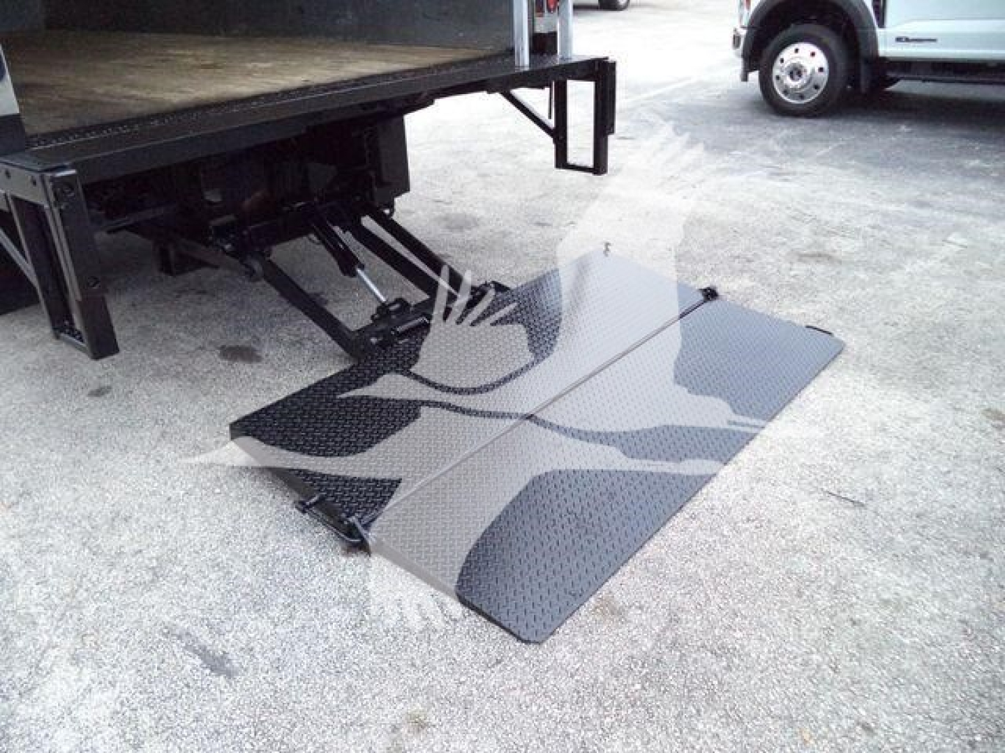 Isuzu NPR-HD truck with a fold-out aluminum loading ramp extended from the back of the box truck. Visible surface shows diamond plate texture.