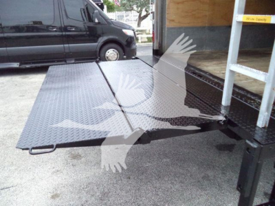 Isuzu NPR HD truck with a metal loading ramp extended from an open box body. The surface shows diamond plate texture.