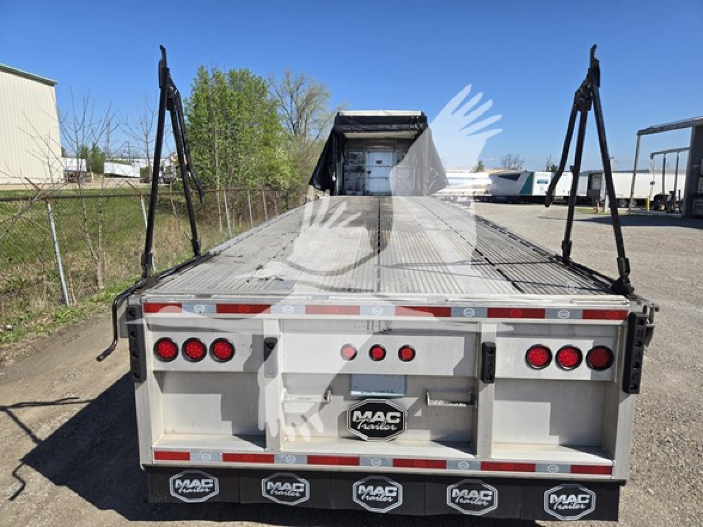 Trailer rear showing aluminum flatbed with MAC trailer logo, taillights, and mud flaps; ramps raised at rear with support posts.