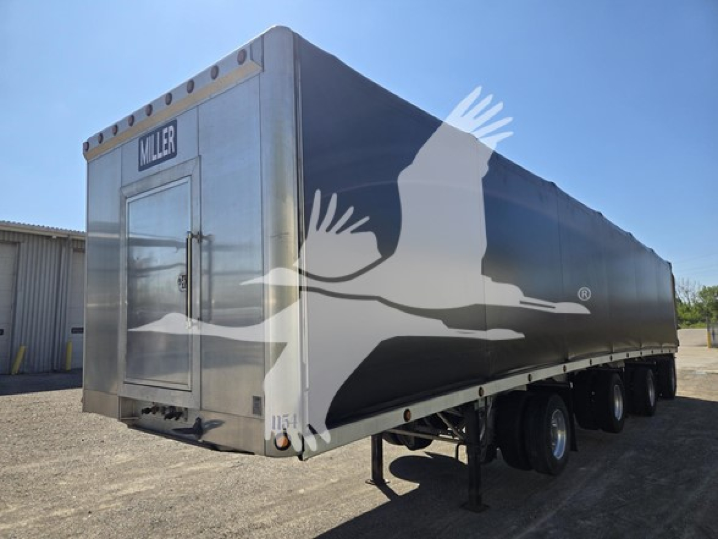 Miller aluminum flatbed trailer with black and gray abstract graphic on side, rear door with Miller logo, tandem axle setup, landing gear visible.